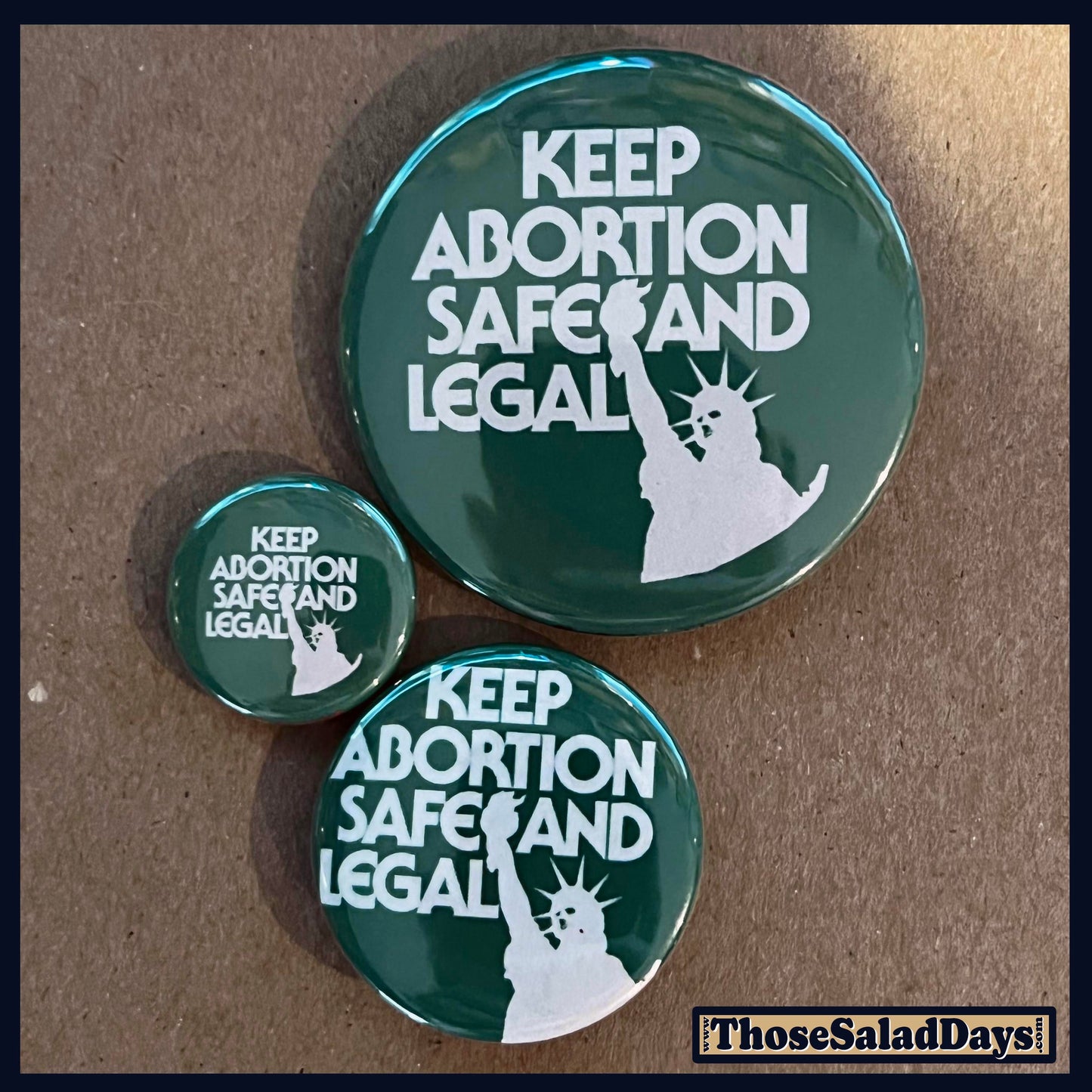 Three green buttons with 'Keep Abortion Safe and Legal' text and a silhouette of the Statue of Liberty on a brown background.