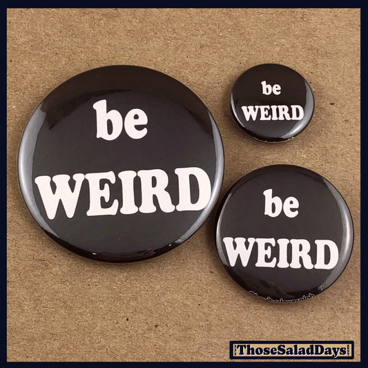 Three 'be WEIRD' buttons on a textured brown background