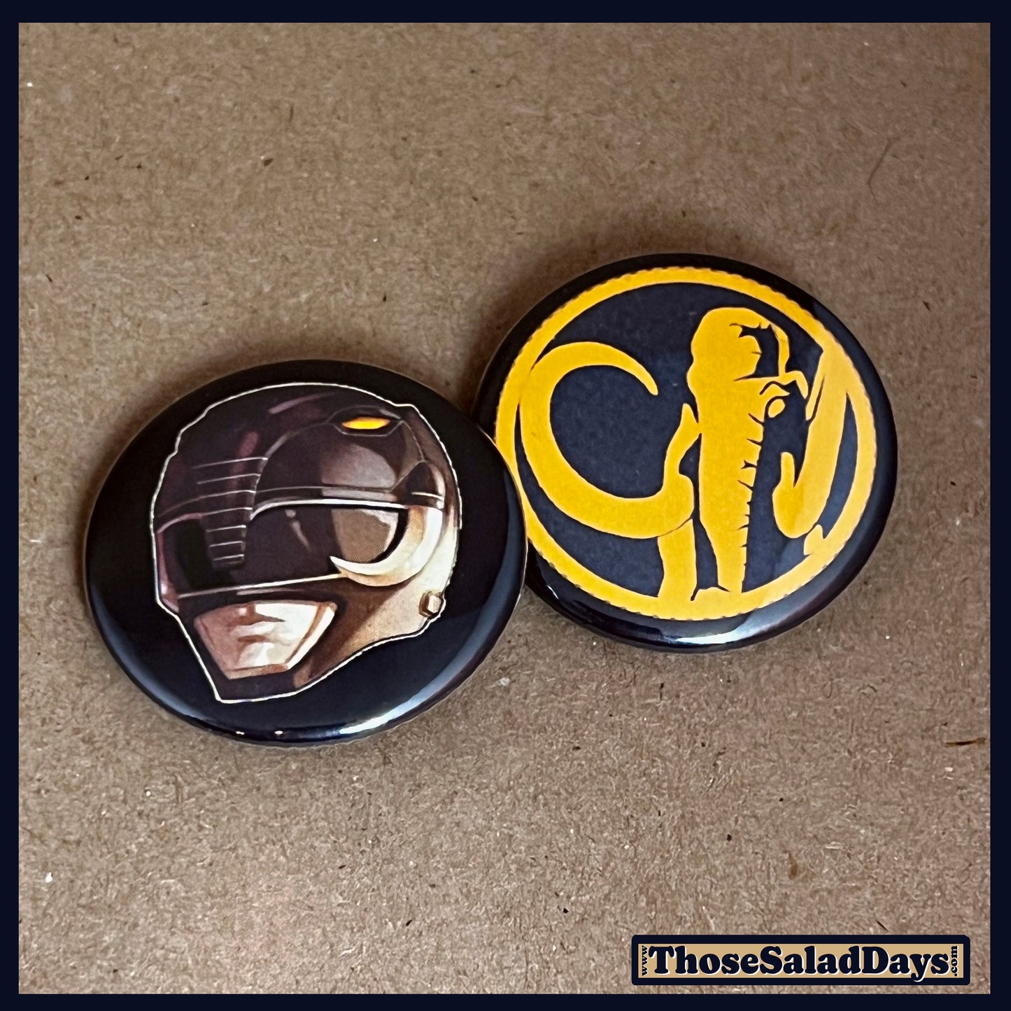 Two buttons featuring a helmet design and dino logo like the Black Power Ranger on a brown background.