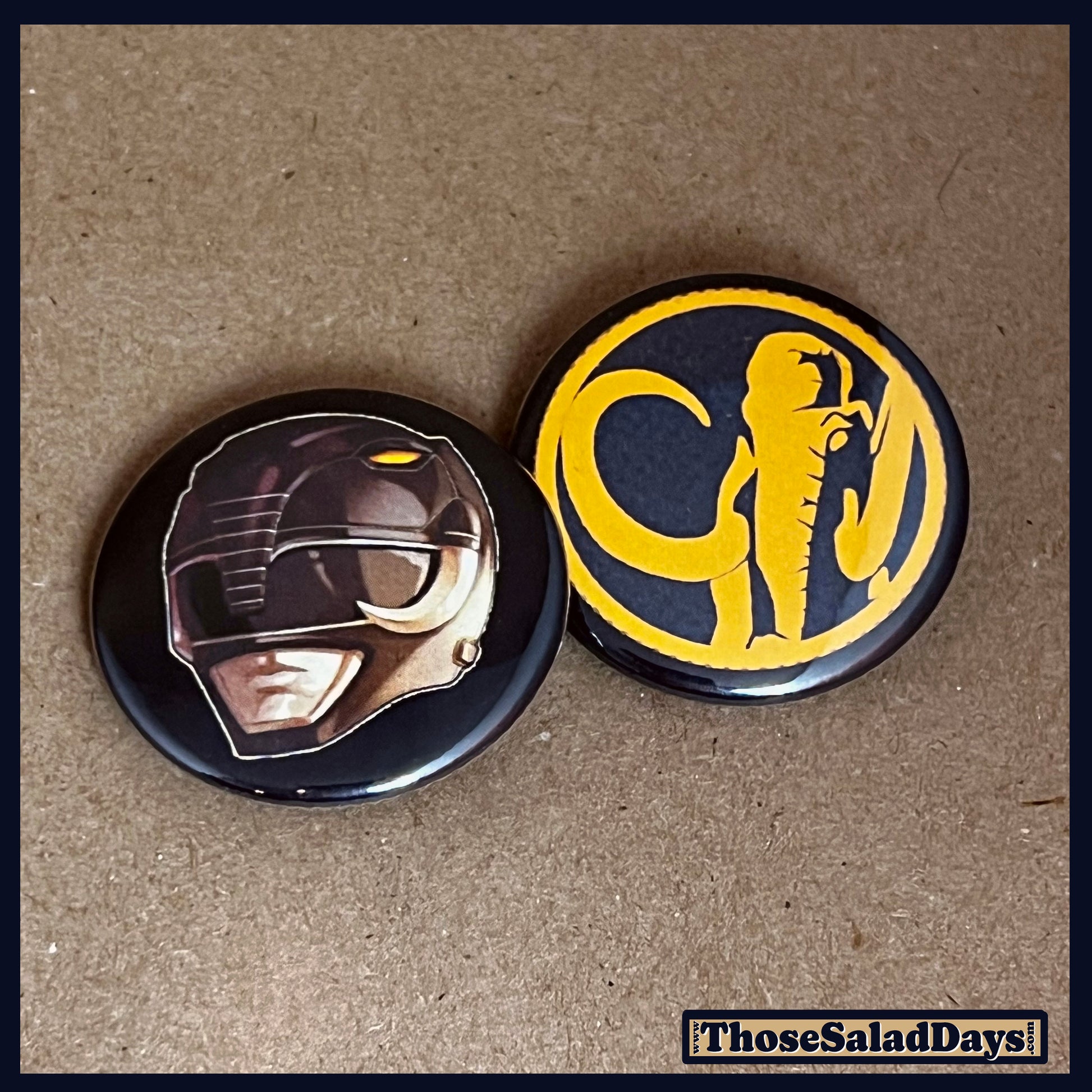 Two buttons featuring a helmet design and dino logo like the Black Power Ranger on a brown background.