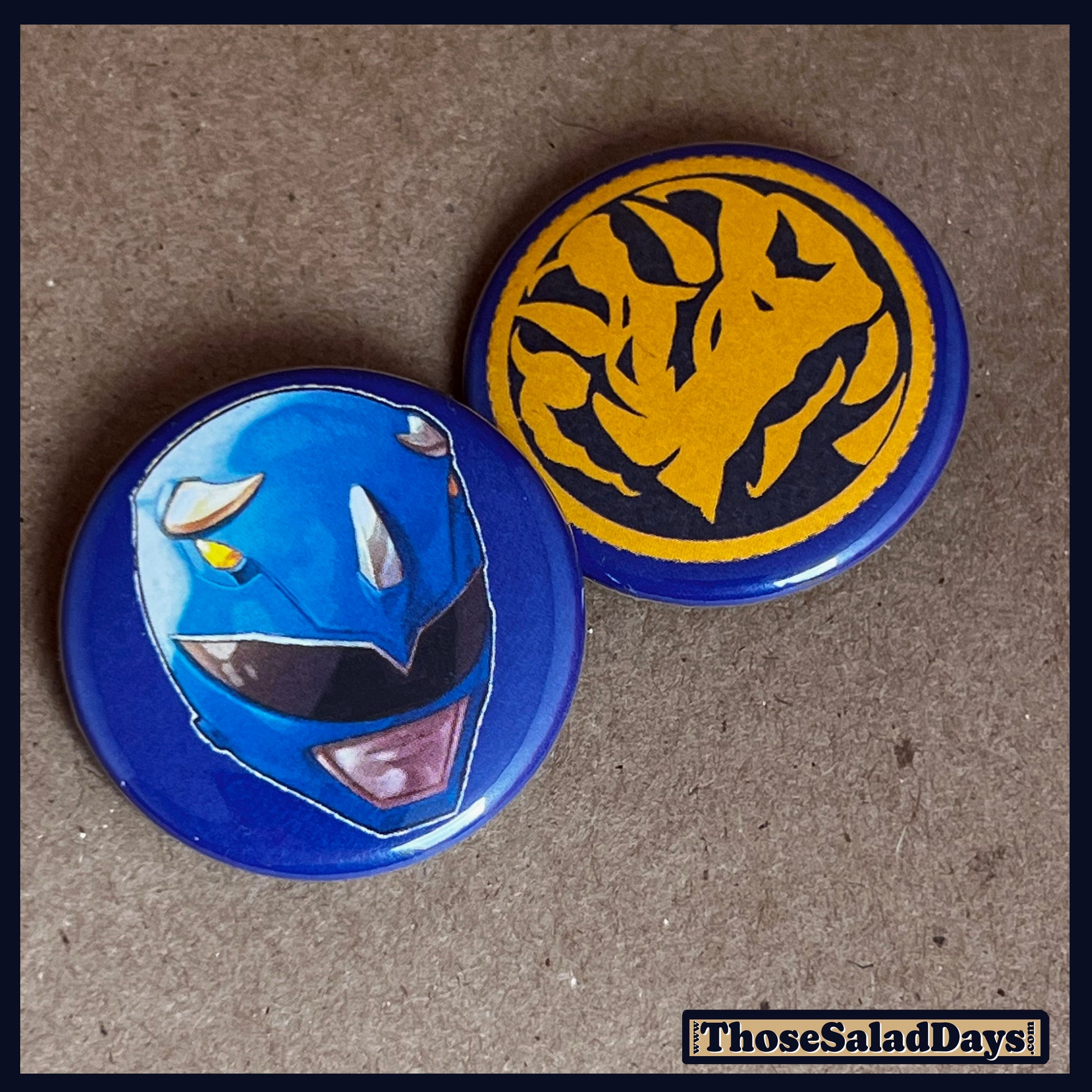 Two buttons featuring a helmet design and dino logo like the Blue Power Ranger on a brown background.