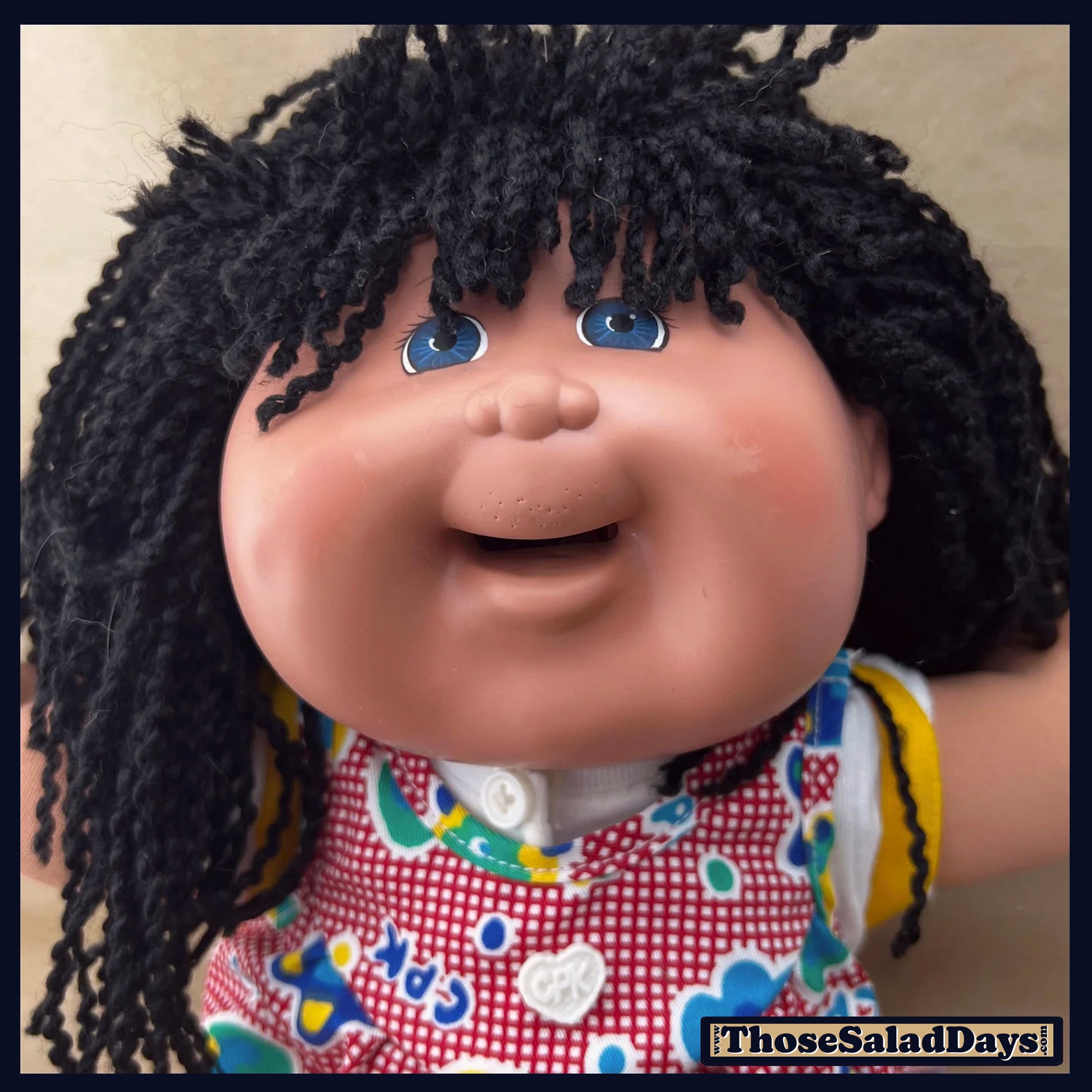 Cabbage Patch Kids doll with black hair and colorful outfit on a beige background