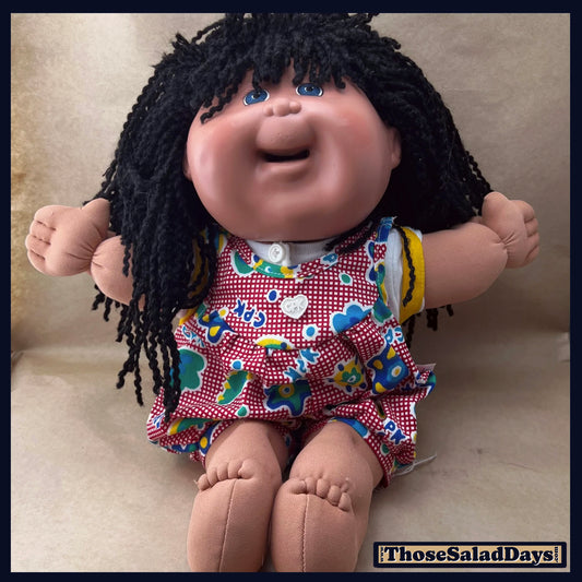 Vintage doll with black hair and colorful outfit on a beige background