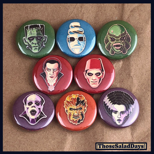 Set of colorful buttons with monster faces on a brown background.