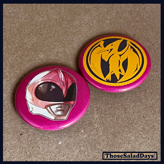Two buttons featuring a helmet design and dino logo like the Pink Power Ranger on a brown background.