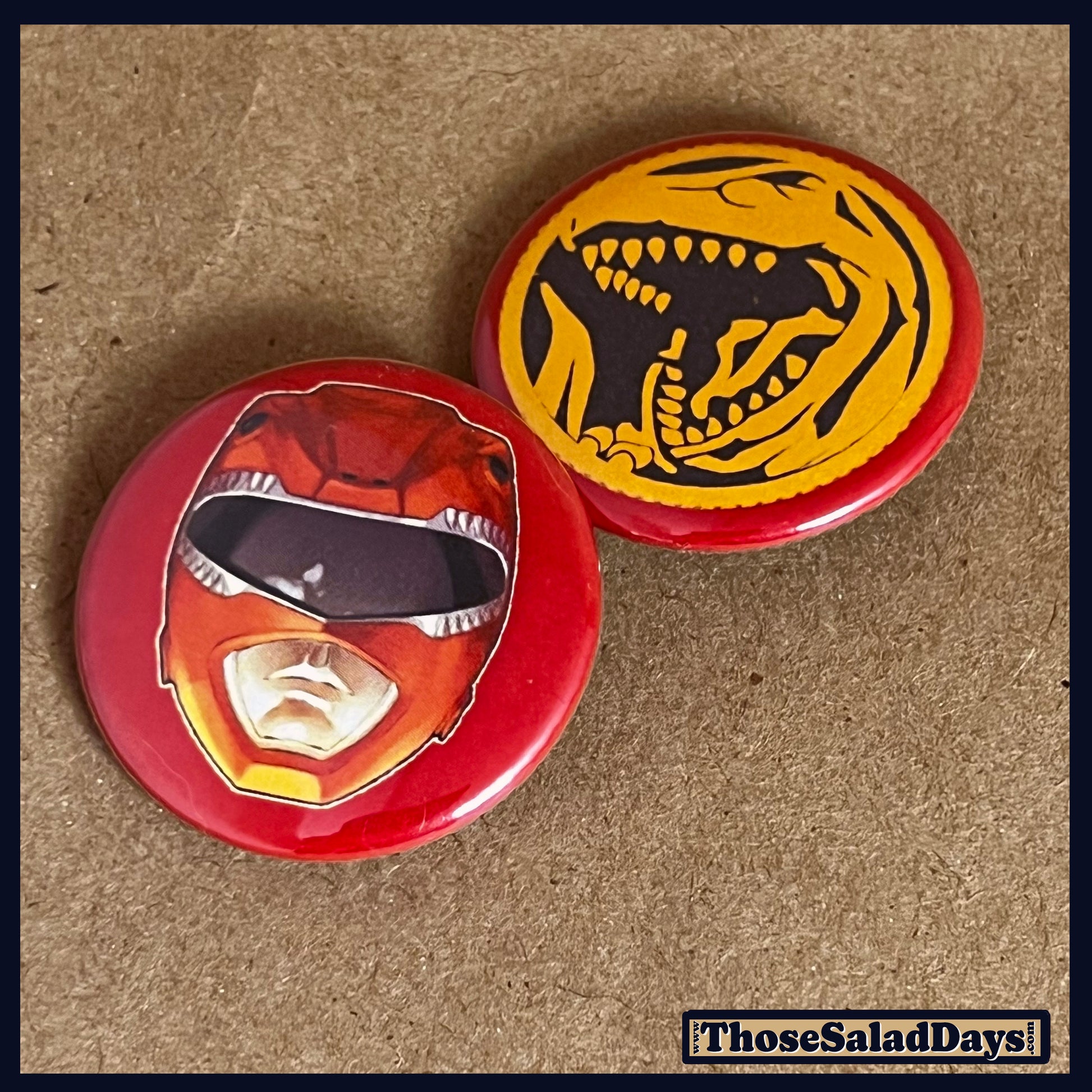 Two buttons featuring a helmet design and dino logo like the Red Power Ranger on a brown background.