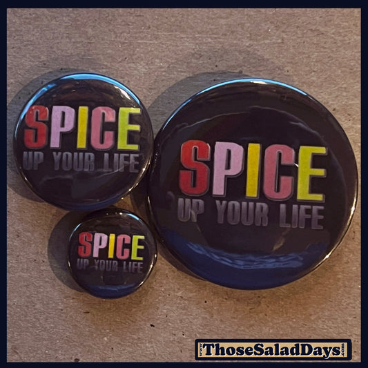 Three 'SPICE UP YOUR LIFE' buttons on a cardboard background