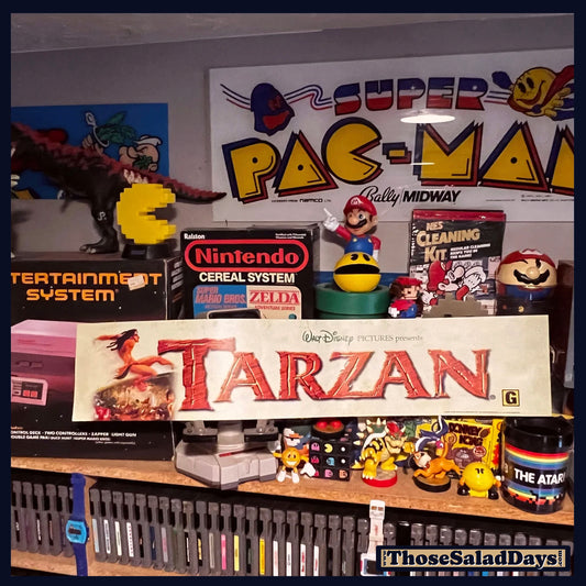 Collection of vintage video game consoles and toys with a 'Super Pac-Man' sign in the background.