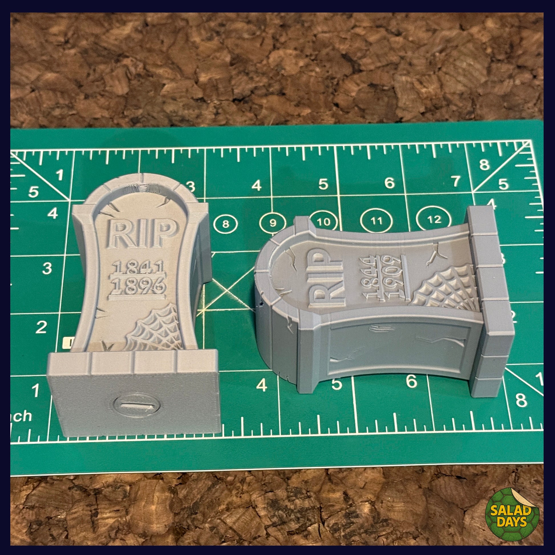 Two miniature tombstones with 'RIP' inscriptions on a green cutting mat.