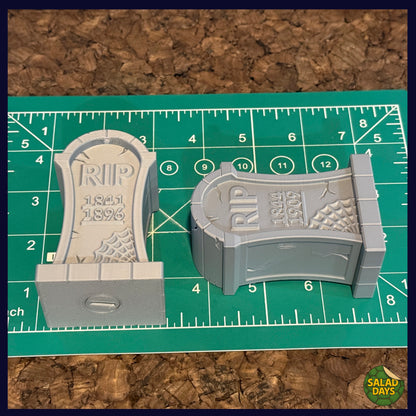 Two miniature tombstones with 'RIP' inscriptions on a green cutting mat.