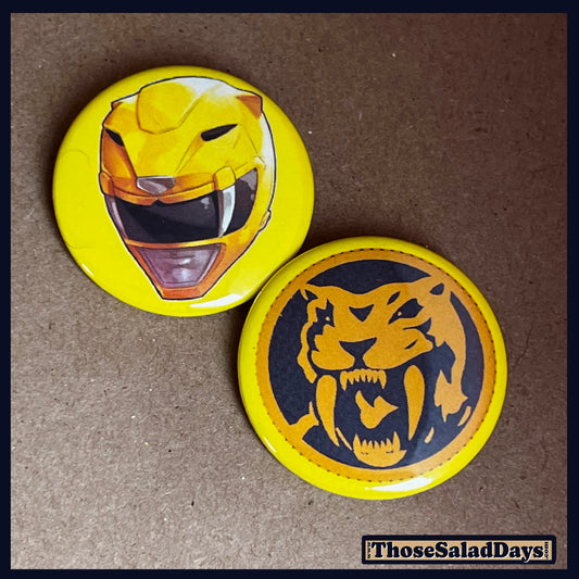 Two buttons featuring a helmet design and dino logo like the Yellow Power Ranger on a brown background.